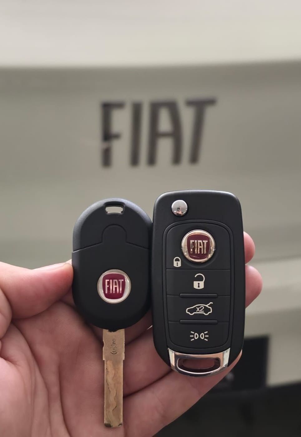 Chave Fiat com lâmina e chave canivete Fiat em frente ao emblema da marca