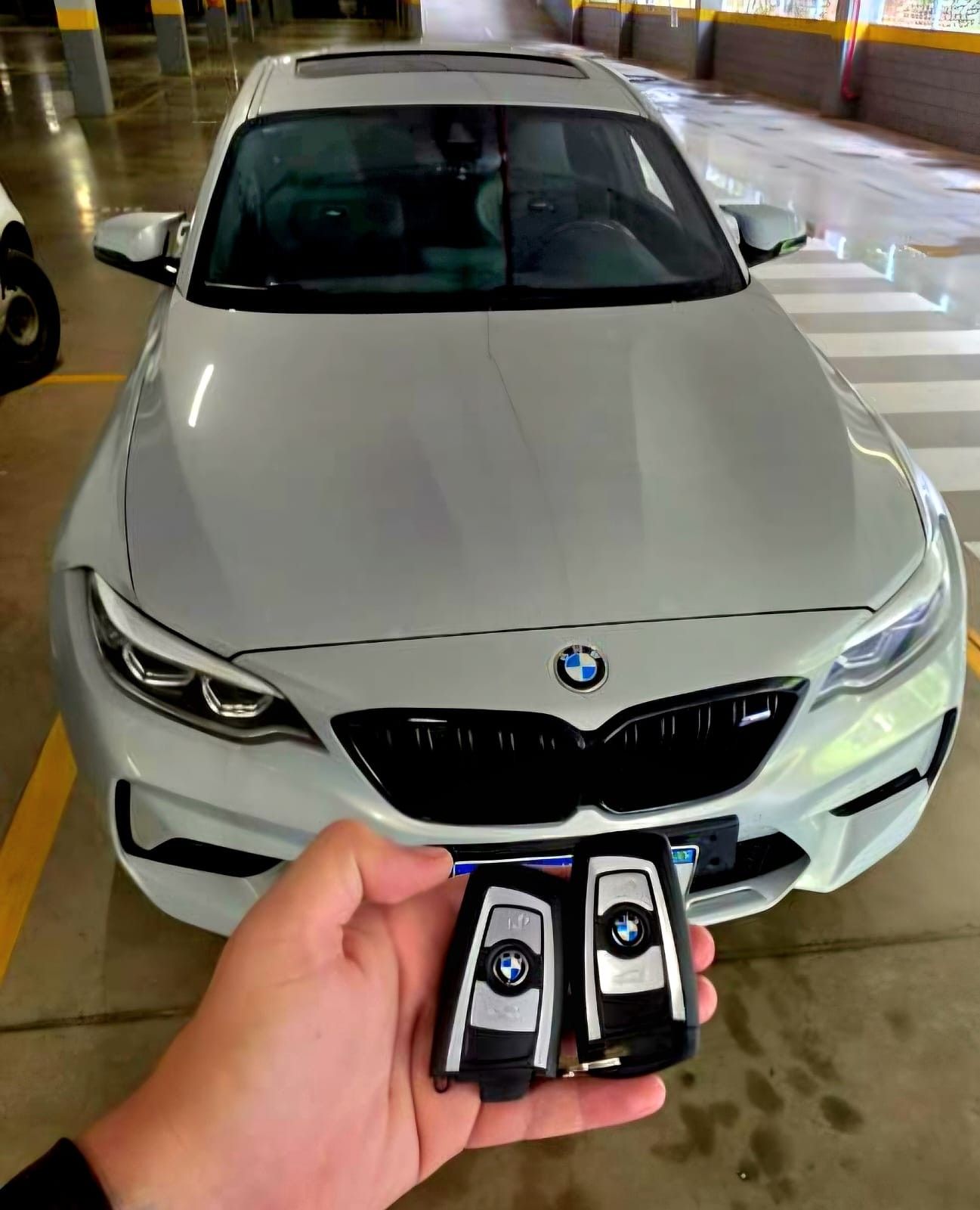 Par de chaves presenciais BMW seguradas em frente a um BMW branco no estacionamento