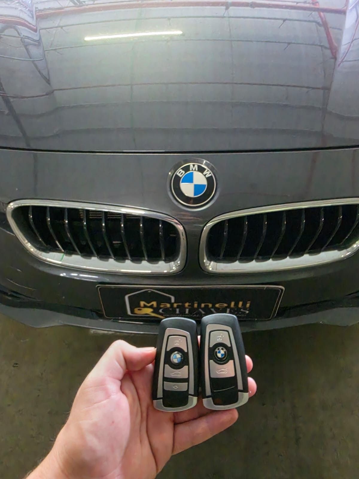 Duas chaves presenciais BMW em frente à grade de um BMW cinza