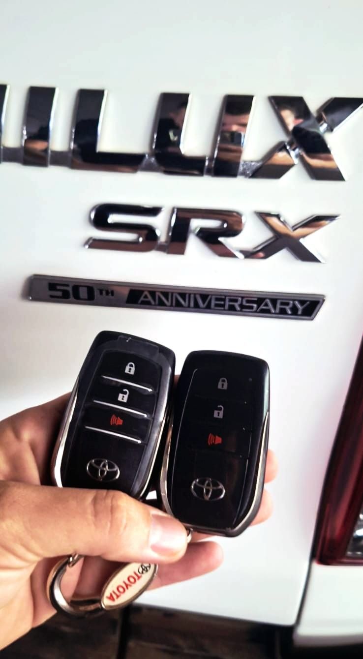 Duas chaves presenciais Toyota em frente à traseira de uma Hilux SRX branca